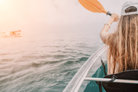 Woman in kayak back view. Happy young woman with long hair floating in transparent kayak on the crystal clear sea. Summer holiday vacation and cheerful female people relaxing having fun on the boatの写真素材