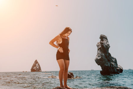 Woman summer travel sea. Happy tourist in hat enjoy taking picture outdoors for memories. Woman traveler posing on the beach at sea surrounded by volcanic mountains, sharing travel adventure journeyの写真素材