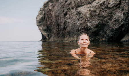Woman travel sea. Happy tourist enjoy taking picture outdoors for memories. Woman traveler swim in the sea bay with mountains, sharing travel adventure journeyの写真素材