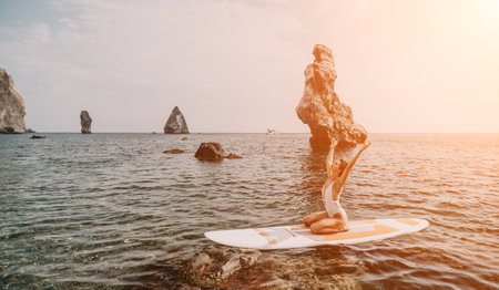 Woman sup yoga. Happy sporty woman practising yoga pilates on paddle sup surfboard. Female stretching doing workout on sea water. Modern individual female hipster outdoor summer sport activity.の写真素材
