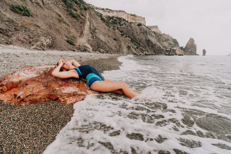 Woman summer travel sea. Happy tourist in blue bikini enjoy taking picture outdoors for memories. Woman traveler posing on the beach surrounded by volcanic mountains, sharing travel adventure journeyの写真素材