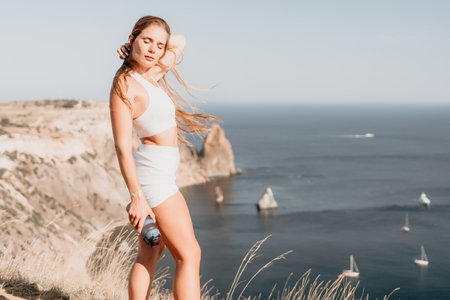 Woman summer travel sea. Happy tourist in hat enjoy taking picture outdoors for memories. Woman traveler posing on the beach at sea surrounded by volcanic mountains, sharing travel adventure journeyの写真素材