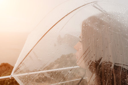 Woman rain umbrella. Happy woman portrait wearing a raincoat with transparent umbrella outdoors on rainy day in park near sea. Girl on the nature on rainy overcast day.の写真素材