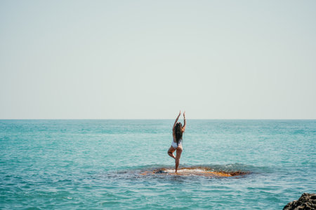 Woman sea yoga. Back view of free calm happy satisfied woman with long hair standing on top rock with yoga position against of sky by the sea. Healthy lifestyle outdoors in nature, fitness conceptの写真素材
