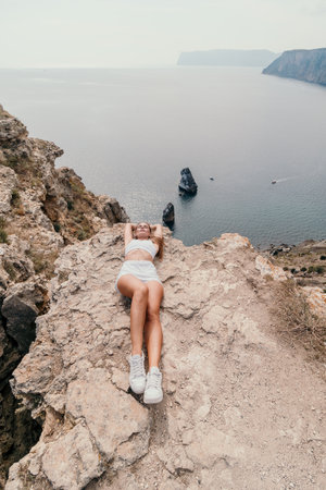 Woman travel sea. Young Happy woman posing on a beach over the sea on background of volcanic rocks, like in Iceland, sharing travel adventure journeyの写真素材