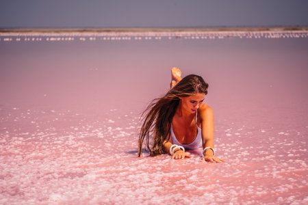 Young woman with long hair in pink salty lake with crystals of salt. Extremely salty pink lake, colored by microalgae with crystalline salt depositions. Spa, beauty and health care concept.の写真素材
