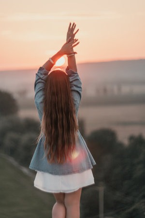 Happy woman standing with her back on the sunset in nature in summer with open hands. Romantic beautiful bride in white boho dress posing with mountains on sunsetの写真素材