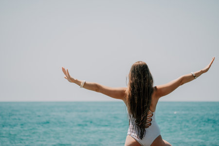 Woman sea yoga. Back view of free calm happy satisfied woman with long hair standing on top rock with yoga position against of sky by the sea. Healthy lifestyle outdoors in nature, fitness concept.の写真素材