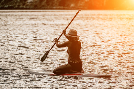 Woman in red bikini on sup board. Happy lady with blond hair in red bathing suit chilling and sunbathing by turquoise sea ocean on sunset. Holiday, vacation and recreational concept.の写真素材
