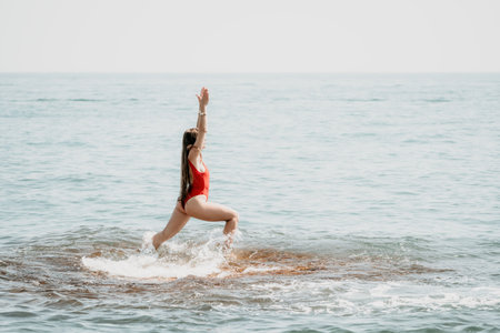 Woman sea yoga. Back view of free calm happy satisfied woman with long hair standing on top rock with yoga position against of sky by the sea. Healthy lifestyle outdoors in nature, fitness conceptの写真素材