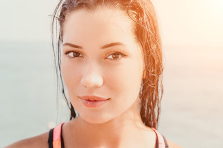 Woman sea sup. Close up portrait of beautiful young caucasian woman with black hair and freckles looking at camera and smiling. Cute woman portrait in a pink bikini posing on sup board in the seaの写真素材