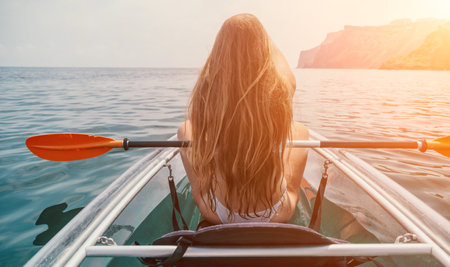 Woman in kayak back view. Happy young woman with long hair floating in transparent kayak on the crystal clear sea. Summer holiday vacation and cheerful female people relaxing having fun on the boatの写真素材