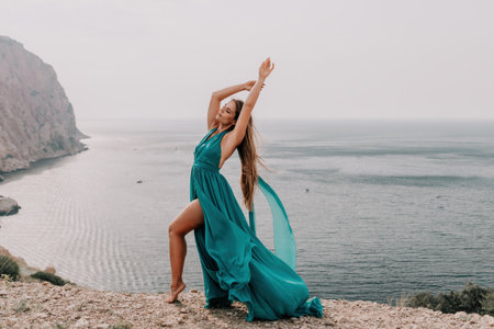 Woman travel portrait. Happy woman with long hair looking at camera and smiling. Close up portrait cute woman in a mint long dress posing on a volcanic rock high above the seaの写真素材