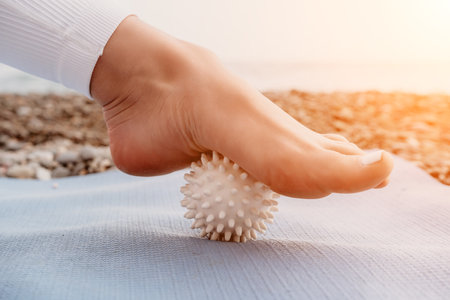Woman sea yoga. Well looking middle aged woman with braids dreadlocks in white leggings and tops doing stretching pilates on yoga mat near sea. Female fitness yoga routine concept. Healthy lifestyle.の写真素材