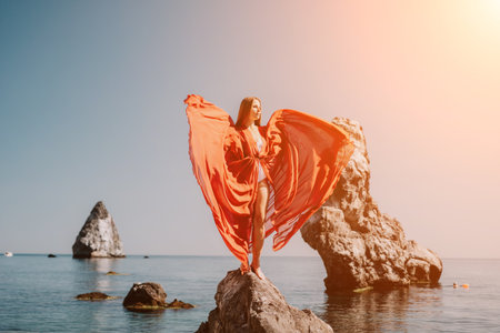 Woman travel sea. Young Happy woman in a long red dress posing on a beach near the sea on background of volcanic rocks, like in Iceland, sharing travel adventure journeyの写真素材
