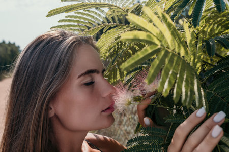 Beauty portrait of happy woman closeup. Young girl smelling Chinese acacia pink blossoming flowers. Portrait of young woman in blooming spring, summer garden. Romantic vibe. Female and natureの写真素材