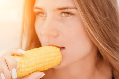 Woman eats corn on beach. Vegetarian hipster woman eat fresh organic grilled corn. Happy lady on sea beach sunset or ocean sunrise. Travel, explore, active yoga and meditation lifestyle concept.の写真素材