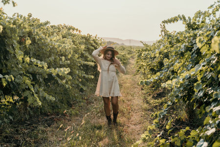 Woman at autumn winery. Portrait of happy woman holding glass of wine and enjoying in vineyard. Elegant young lady in hat toasting with wineglass smiling cheerfully enjoying her stay at vineyard.の写真素材