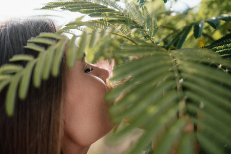 Beauty portrait of happy woman closeup. Young girl smelling Chinese acacia pink blossoming flowers. Portrait of young woman in blooming spring, summer garden. Romantic vibe. Female and natureの写真素材