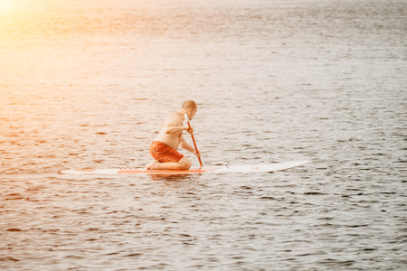 Active mature male paddler with his paddleboard and paddle on a sea at summer. Happy senior man stands with a SUP board. Stand up paddle boarding - outdor active recreation in nature.の写真素材