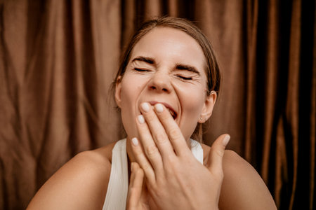 Yawning middle aged woman in white t-shirt, feeling lack of sleep, fatigue, and boredom. Female Wake up at her house early morning.の写真素材