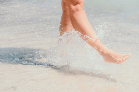 Sea beach travel - woman walking on sand beach leaving footprints in the white sand. Female legs walking along the seaside barefoot, close-up of the tanned legs of a girl coming out of the water.の写真素材