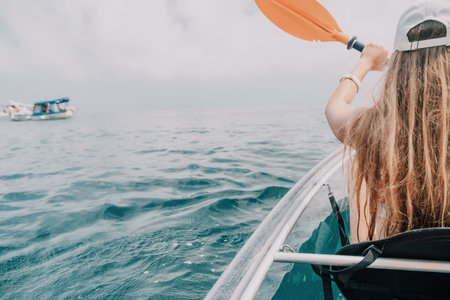Woman in kayak back view. Happy young woman with long hair floating in transparent kayak on the crystal clear sea. Summer holiday vacation and cheerful female people relaxing having fun on the boatの写真素材