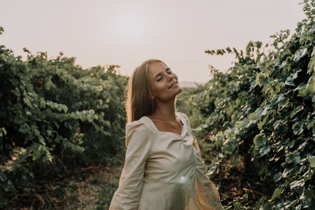 Woman picnic vineyard. Happy woman with a glass of wine at a picnic in the vineyard, wine tasting at sunset and open nature in the summer. Romantic dinner, fruit and wine.の写真素材