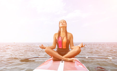 Woman sup yoga. Happy young sporty woman practising yoga pilates on paddle sup surfboard. Female stretching doing workout on sea water. Modern individual female outdoor summer sport activity.の写真素材