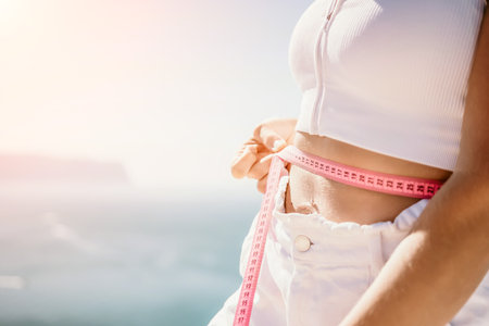 woman in white shorts holds in her hands pink measuring tape on her waist near the azure sea. Concept of detox and dietの写真素材