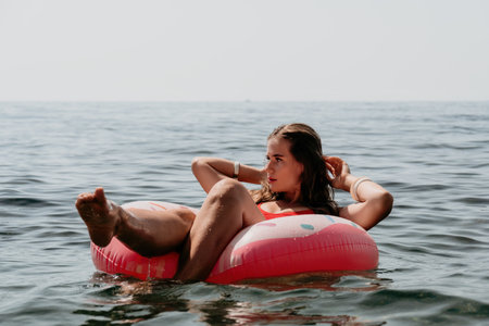 Woman summer sea. Happy woman swimming with inflatable donut on the beach in summer sunny day, surrounded by volcanic mountains. Summer vacation concept.の写真素材