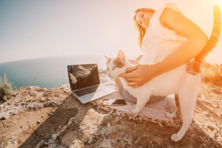 Woman sea laptop. Business woman petting cat and working on laptop by the sea. Close up on hands of pretty lady typing on computer outdoors summer day. Freelance, digital nomad and holidays concept.の写真素材