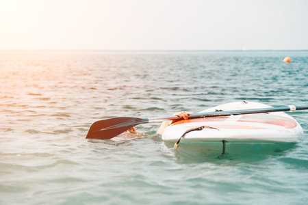 Sea woman sup. Silhouette of happy young woman in pink bikini, surfing on SUP board, confident paddling through water surface. Idyllic sunset. Active lifestyle at sea or river.の写真素材