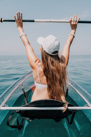 Woman in kayak back view. Happy young woman with long hair floating in transparent kayak on the crystal clear sea. Summer holiday vacation and cheerful female people relaxing having fun on the boatの写真素材