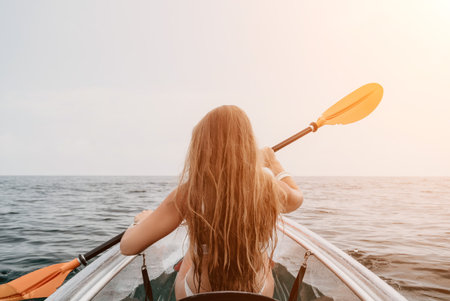 Woman in kayak back view. Happy young woman with long hair floating in transparent kayak on the crystal clear sea. Summer holiday vacation and cheerful female people relaxing having fun on the boatの写真素材