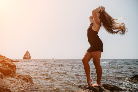 Woman summer travel sea. Happy tourist in hat enjoy taking picture outdoors for memories. Woman traveler posing on the beach at sea surrounded by volcanic mountains, sharing travel adventure journeyの写真素材