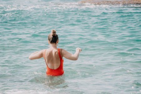 Young woman in red bikini on Beach. Happy lady in bathing suit chilling and sunbathing by turquoise sea ocean on hot summer day. Close up. Back viewの写真素材