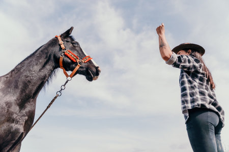 Young happy woman in hat with her horse in evening sunset light. Outdoor photography with fashion model girl. Lifestyle mood. Concept of outdoor riding, sports and recreation.の写真素材