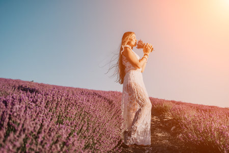 Woman lavender field. Happy carefree woman in a white dress walking in a lavender field and smelling a lavender bouquet on sunset. Ideal for warm and inspirational concepts in wanderlust and travel.の写真素材