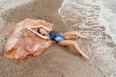 Woman summer travel sea. Happy tourist in blue bikini enjoy taking picture outdoors for memories. Woman traveler posing on the beach surrounded by volcanic mountains, sharing travel adventure journeyの写真素材