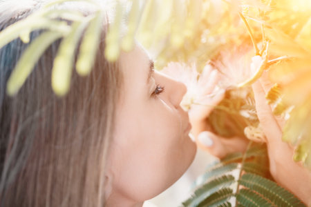 Beauty portrait of happy woman closeup. Young girl smelling Chinese acacia pink blossoming flowers. Portrait of young woman in blooming spring, summer garden. Romantic vibe. Female and natureの写真素材