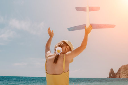 Kid playing with toy airplane. Children dream of travel by plane. Happy child girl has fun in summer vacation by sea and mountains. Outdoors activities at background of blue sky. Lifestyle moment.の写真素材