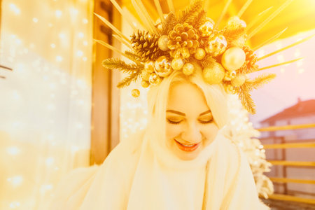 A woman in a white dress is holding a gold box with a red ribbon. She is wearing a crown on her head. The woman appears to be opening the gift box.の写真素材