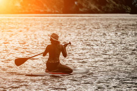 Woman in red bikini on sup board. Happy lady with blond hair in red bathing suit chilling and sunbathing by turquoise sea ocean on sunset. Holiday, vacation and recreational concept.の写真素材