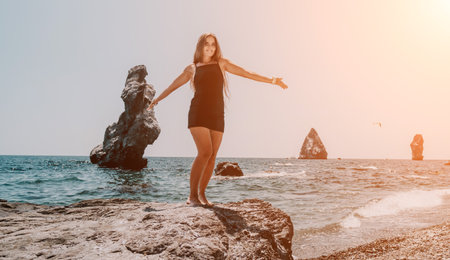 Woman summer travel sea. Happy tourist in hat enjoy taking picture outdoors for memories. Woman traveler posing on the beach at sea surrounded by volcanic mountains, sharing travel adventure journeyの写真素材