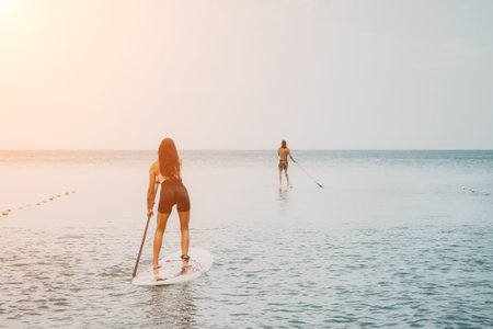 Sea woman and man on sup. Silhouette of happy young woman and man, surfing on SUP board, confident paddling through water surface. Idyllic sunset. Active lifestyle at sea or river.の写真素材