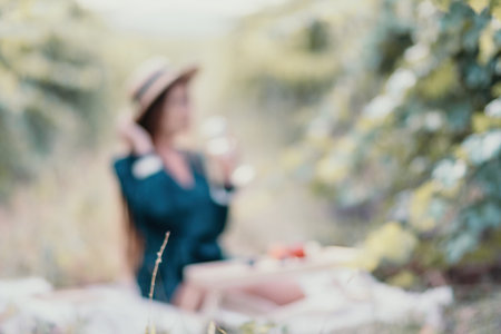 Abstract defocused woman picnic vineyard. Happy woman with a glass of wine at a picnic in the vineyard, wine tasting at sunset and open nature in the summer. Romantic dinner, fruit and wine.の写真素材