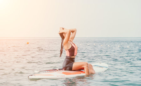 Sea woman sup. Silhouette of happy young woman in pink bikini, surfing on SUP board, confident paddling through water surface. Idyllic sunset. Active lifestyle at sea or river.の写真素材