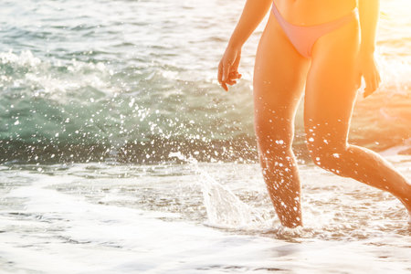 Running woman on a summer beach. A woman jogging on the beach at sunrise, with the soft light of the morning sun illuminating the sand and sea, evoking a sense of renewal, energy and health.の写真素材