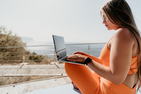 Woman laptop sea. Working remotely on seashore. Happy successful woman female freelancer working on laptop by the sea at sunset, makes a business transaction online. Freelance, remote work on vacationの写真素材